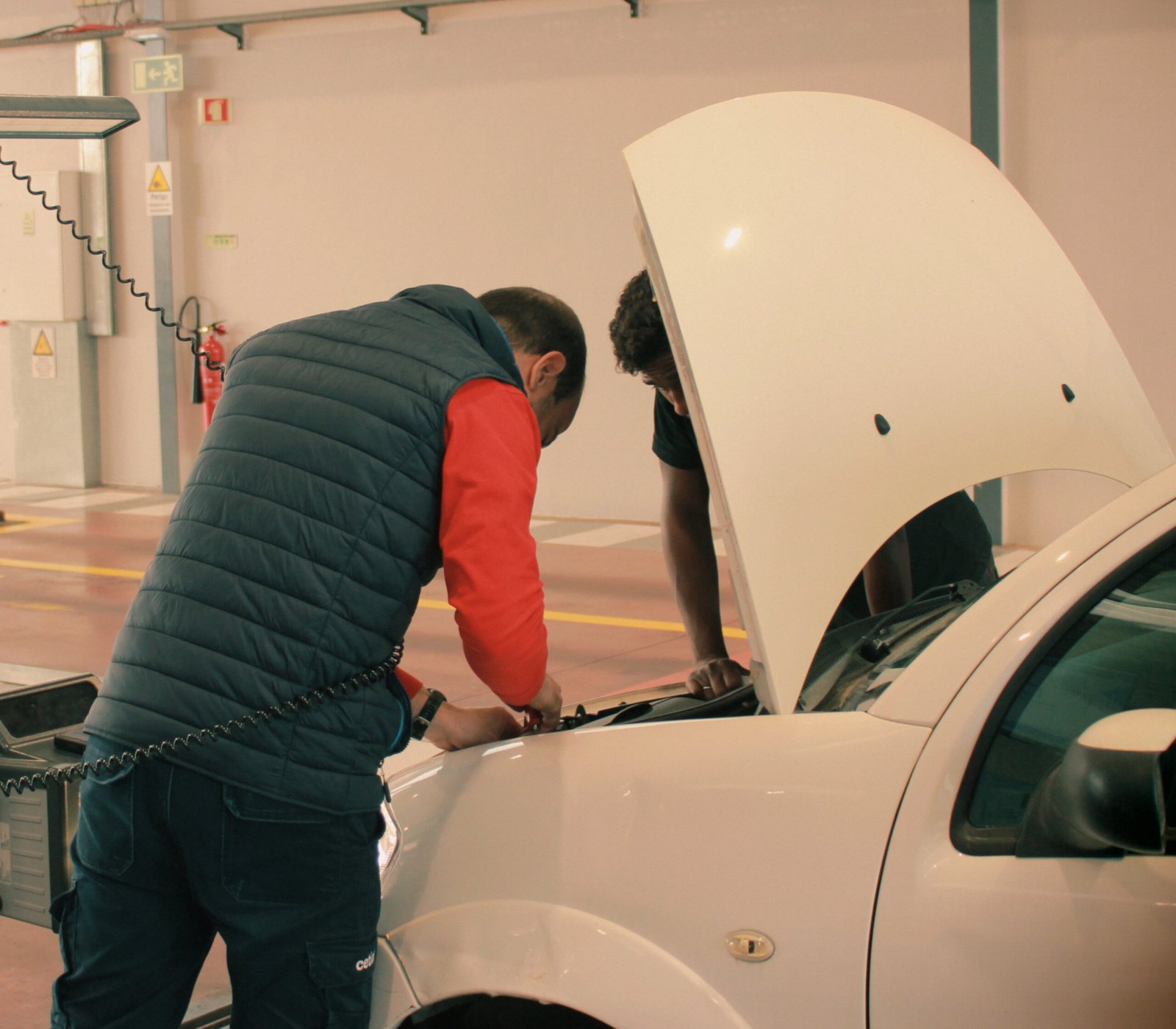 Técnico realiza a inspeção extraordinária em um automóvel de um carro com o capô aberto, verificando os componentes mecânicos numa oficina.