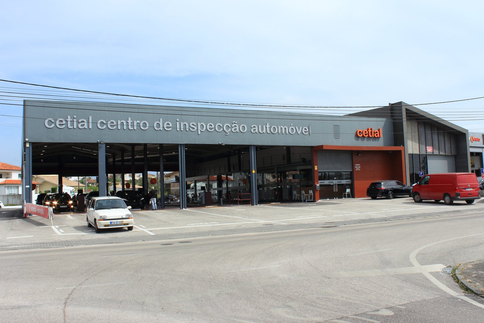 Fachada do CETIAL – Centro de Inspeção Automóvel, com veículos estacionados na entrada e a via pública em primeiro plano. Entre em contacto conosco.